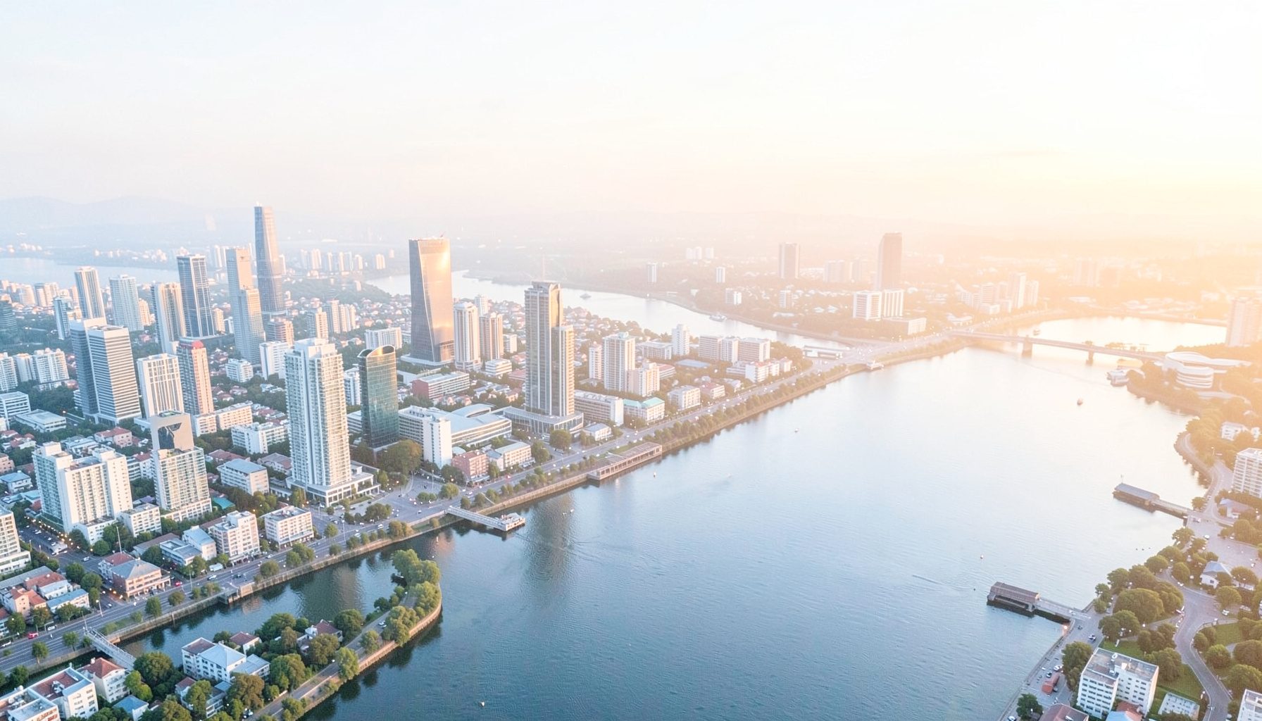 Aerial rendering of a modern city skyline at dusk beside a wide river, with soft amber and pale blue tones